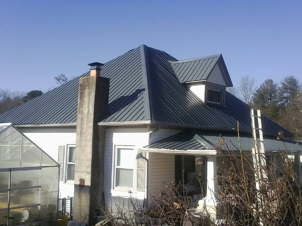 Dark blue standing seam metal roof on a white farmhouse with dormer — Slate & Tile Roof Repair by Roofing Brothers in Babson Park