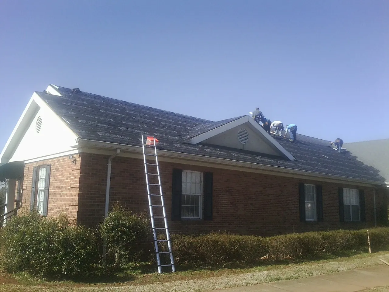 Crew tearing shingles off a brick ranch roof with a ladder set — Emergency Roof Repair work by our crew in Babson Park