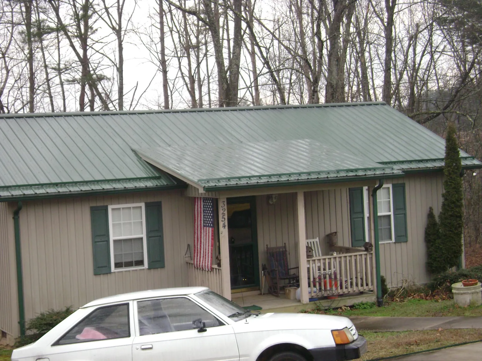 Green metal roof and front porch on a tan sided cottage in Babson Park