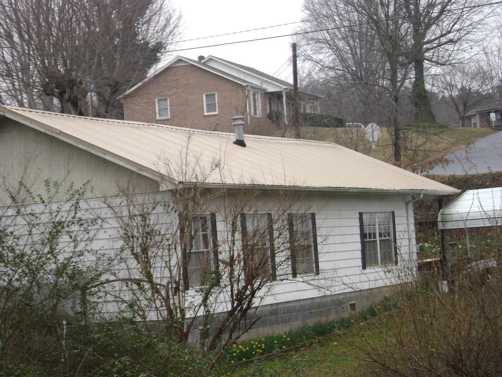 Tan metal roof on a white sided house set into a hillside — Commercial Roofing by Roofing Brothers in Babson Park